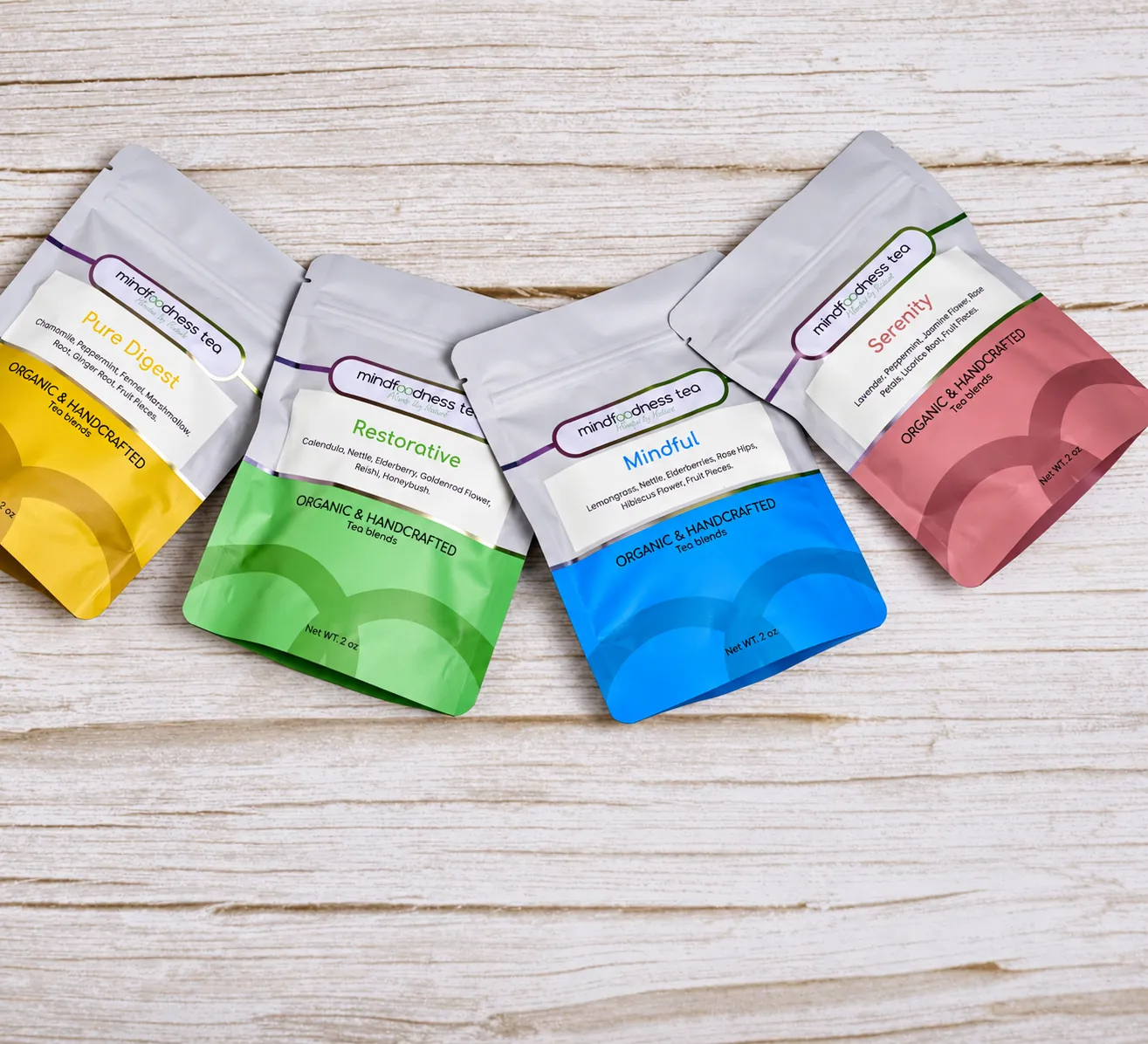 Four Mindfoodness Tea pouches in yellow, green, blue and pink on a wooden table Four Mindfoodness Tea pouches in yellow, green, blue and pink on a wooden table
