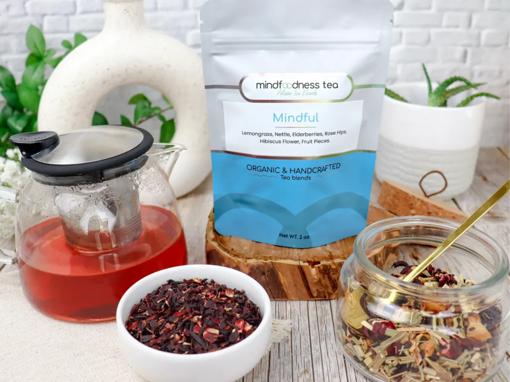 Mindful Tea pouch with a glass teapot of ruby tea and dried hibiscus