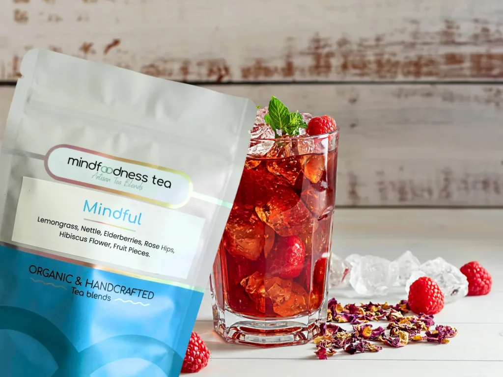 Mindful Tea pouch with lemongrass, nettle, elderberries, rose hips and hibiscus next to a glass of ruby-red iced tea